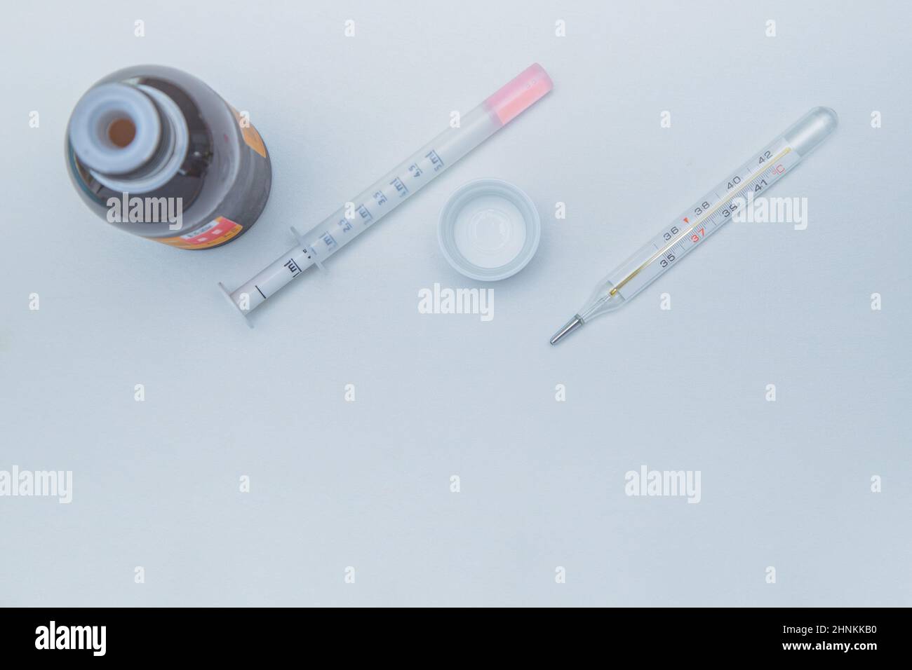 A medicine with a measuring syringe and a thermometer lies a white