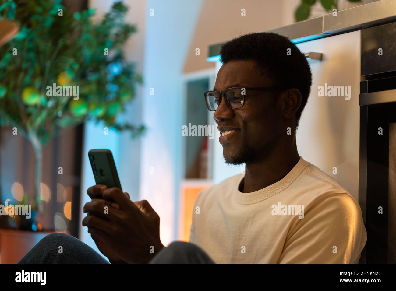 Young happy black guy using smartphone while relaxing and spending leisure time at cozy home Stock Photo