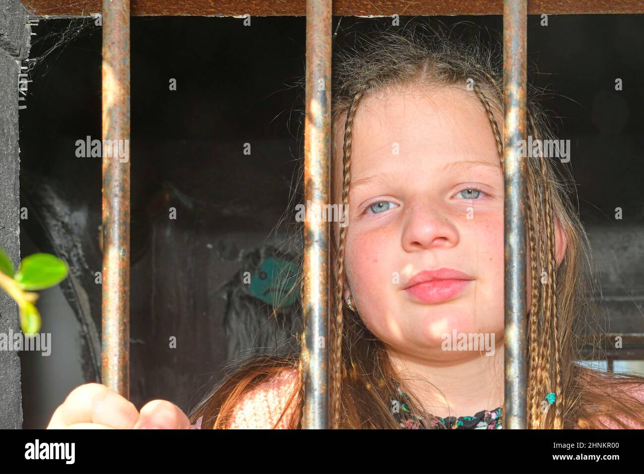 Photo of a little girl holding bars. Sad little girl behind iron bars. Little girl behind the bars. Violence concept Stock Photo