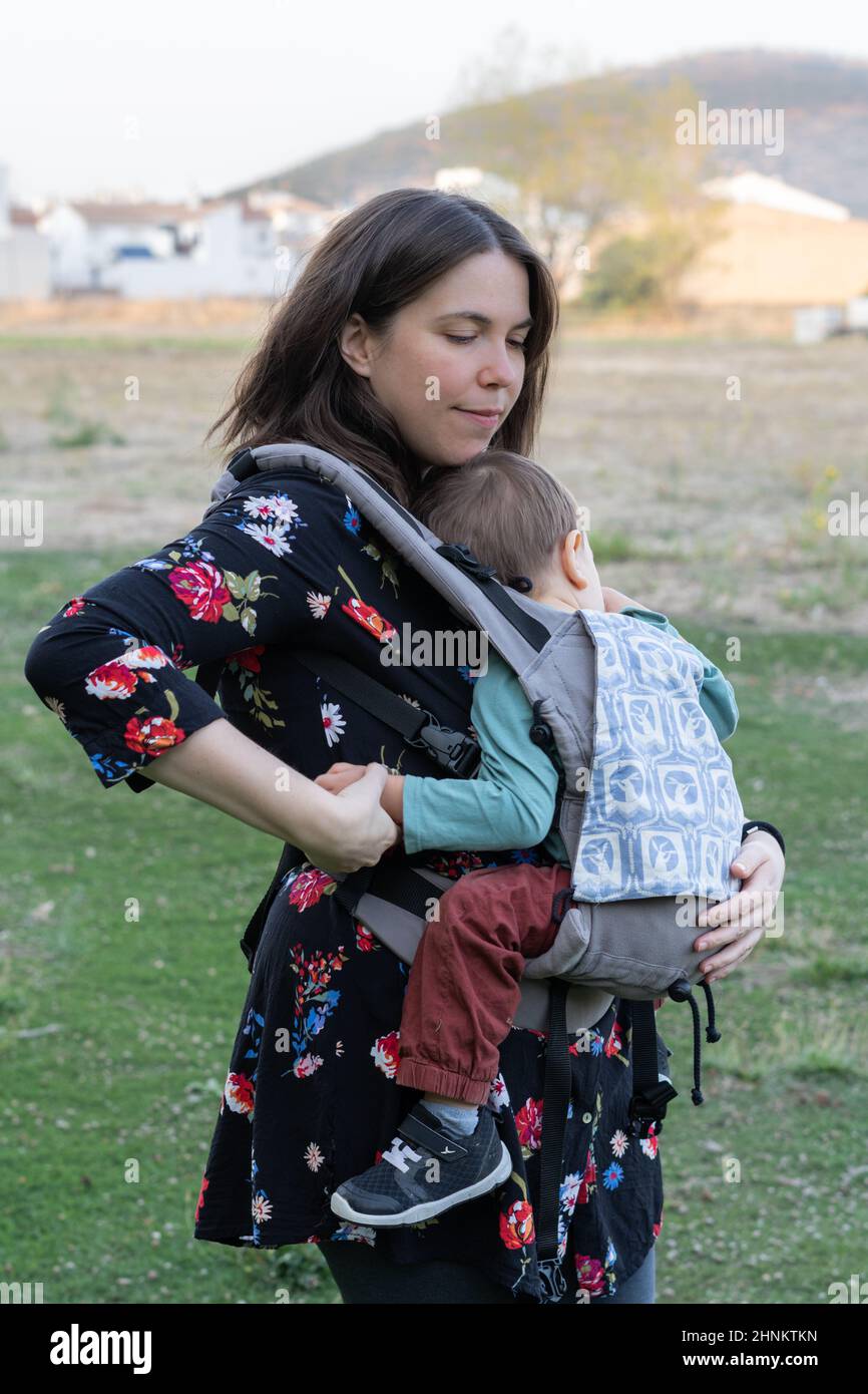 Mother smiling in park with baby in sling Stock Photo