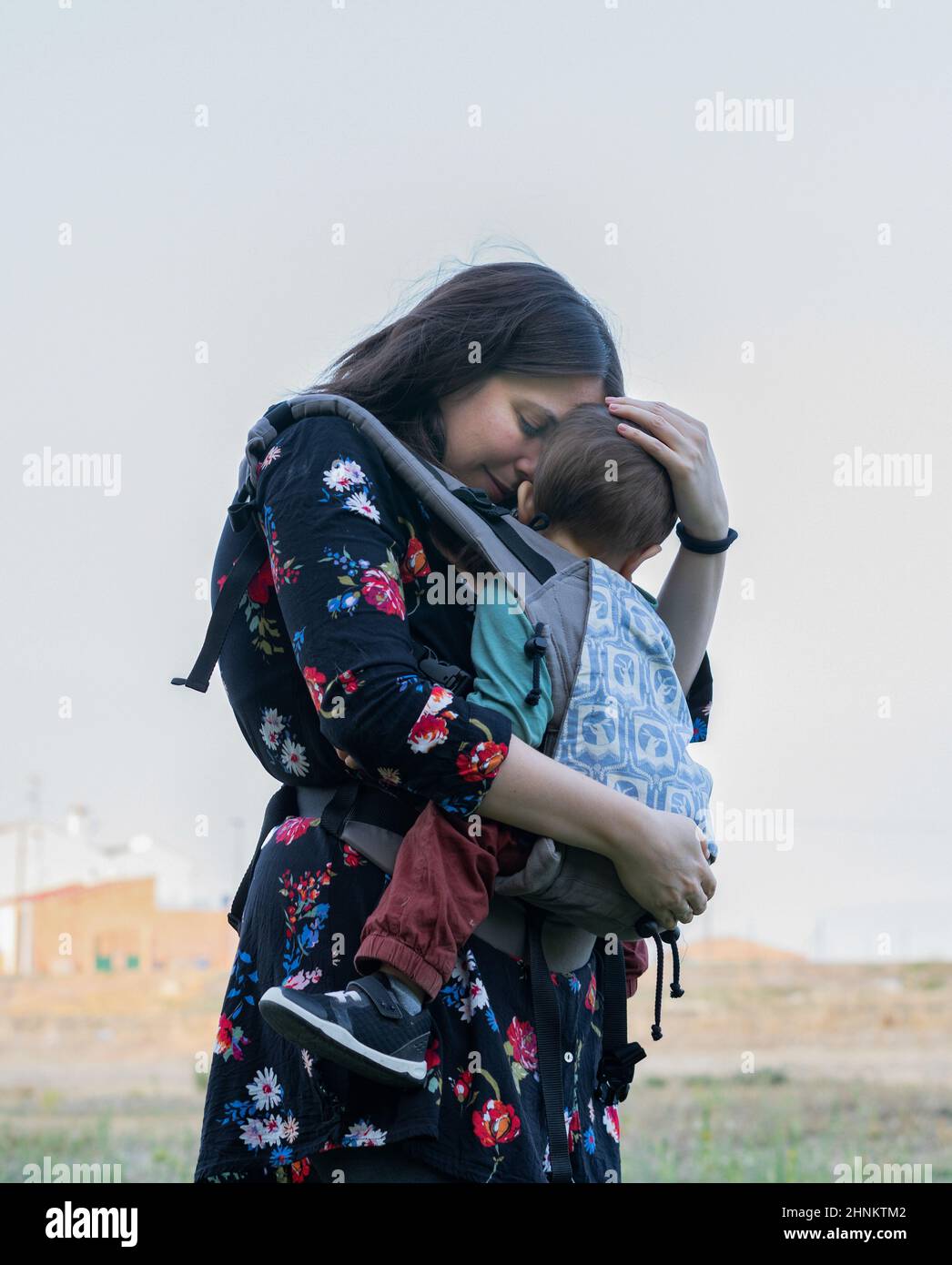 Mother smiling in park with baby in sling Stock Photo