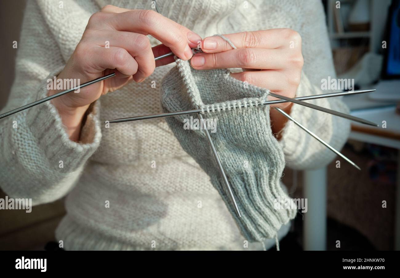 Cozy knitting woman in knitted warm sweater enjoys knit work at home in