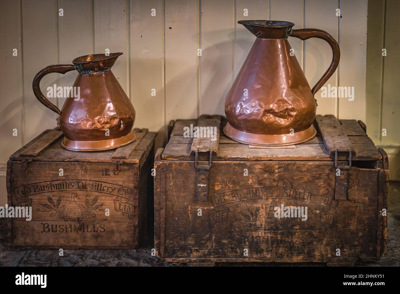 Vintage copper jugs standing on wooden crates with Bushmills whiskey bandings Stock Photo