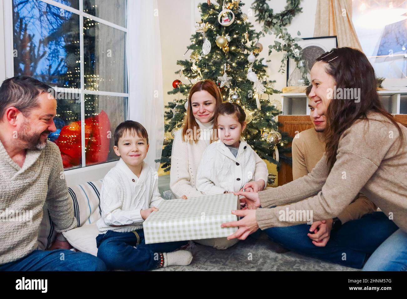 Big happy family with children gathering at home around New Years festive tree. Joyful parents, grandparents and little kids exchanging Christmas gift Stock Photo