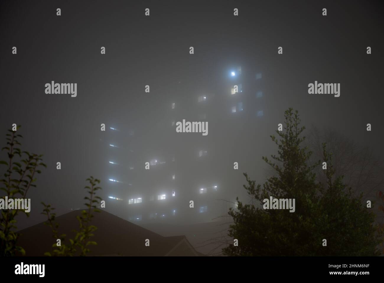 Eerie sky scraper hospital lights shine through very thick fog. Stock Photo