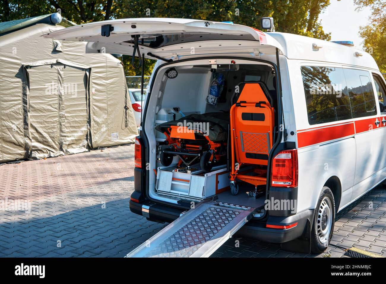 Opened back door of ambulance vehicle, bright orange carrying stretcher and chair visible Stock Photo
