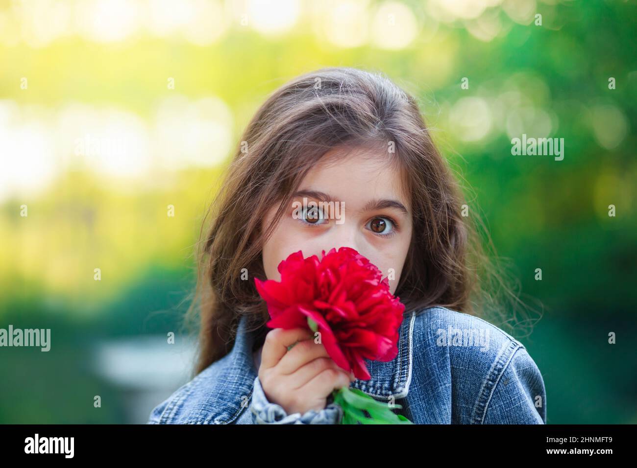 Surprised Little cute girl with peony flowers. Child  playing in summer garden. Kids gardening. Children with flower bouquet for birthday or mother s Stock Photo