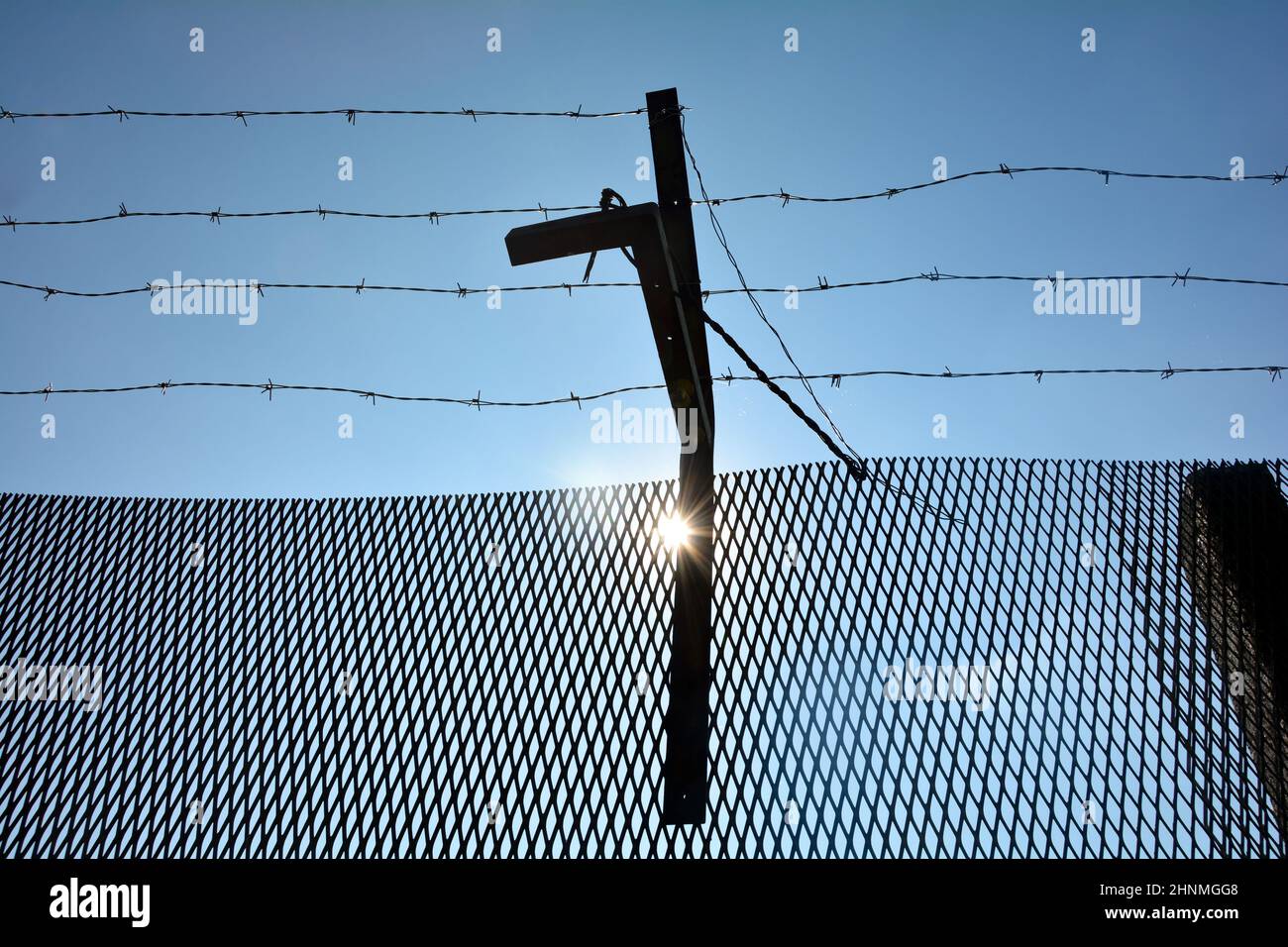 A metal fence with barbed wire , blue sky and sun Stock Photo - Alamy