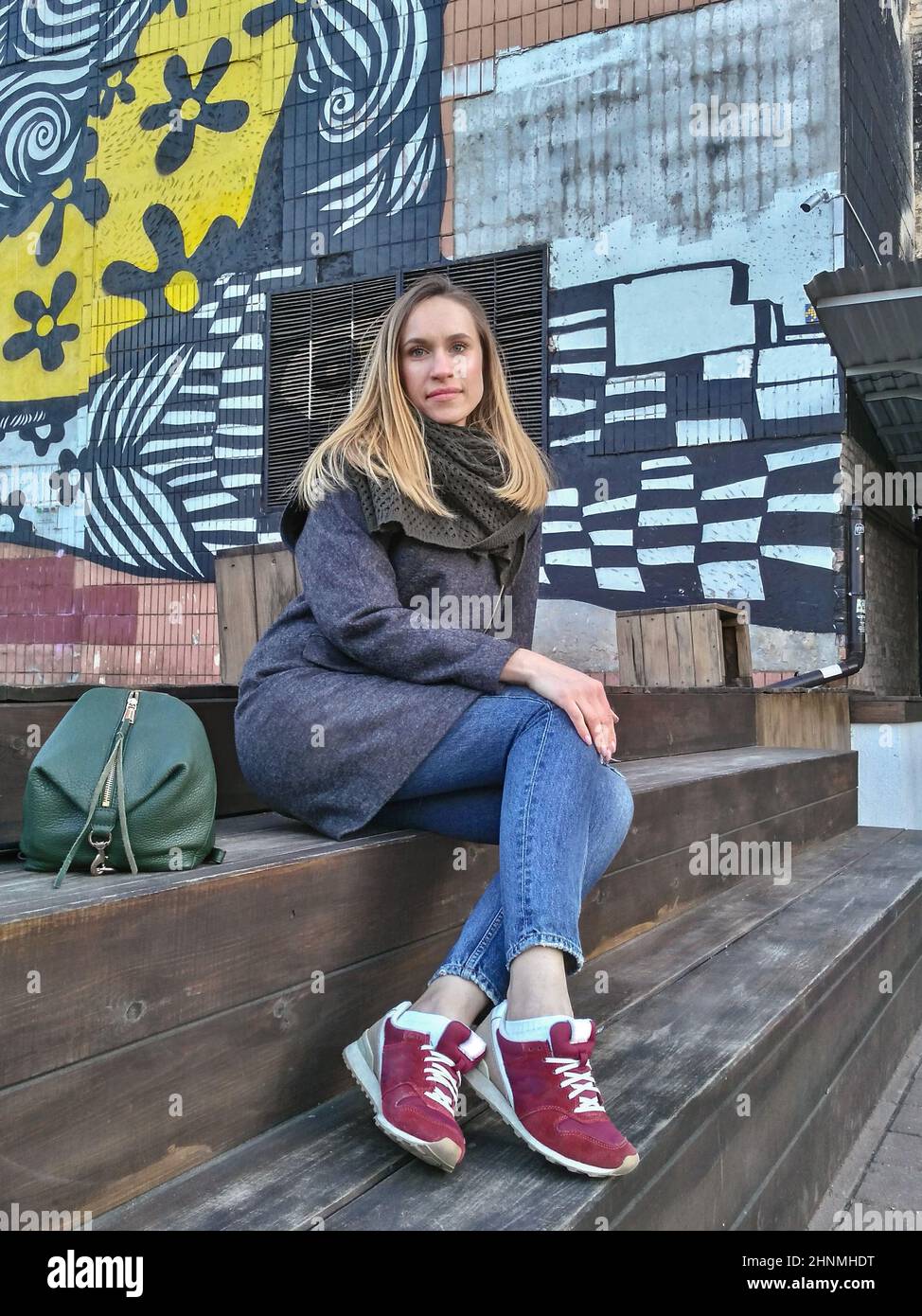 A young woman looks directly into the camera against the backdrop of a painted wall in the fall Stock Photo