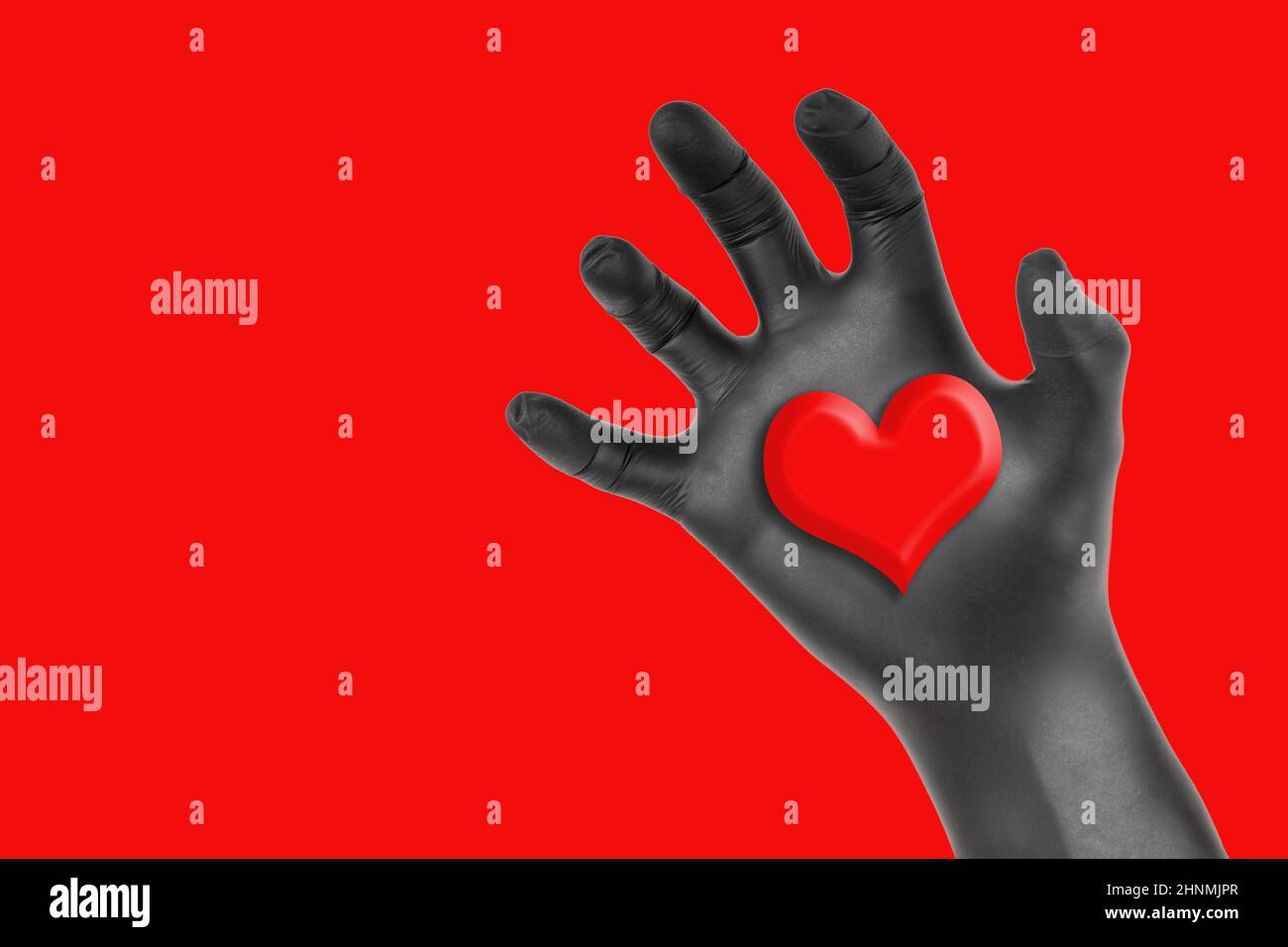 Black gloved hand grabbing a heart isolated on a red background. Romantic heart stealing concept. Stock Photo