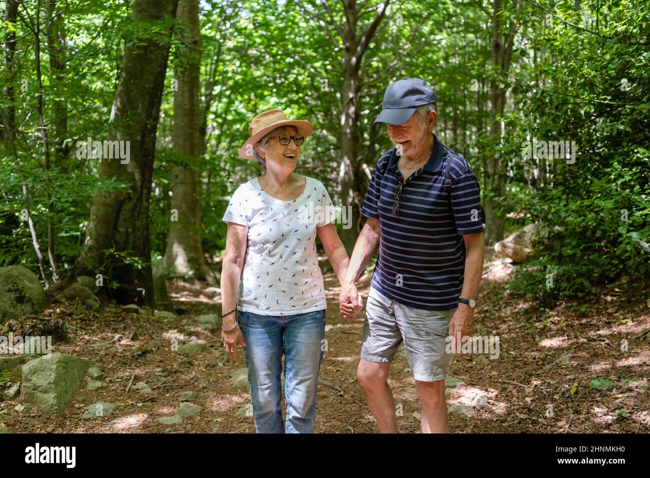 Healthy senior couple walking in a beautiful, sunny forest in summer, laughing; concept: active retirement, healthy lifestyle Stock Photo
