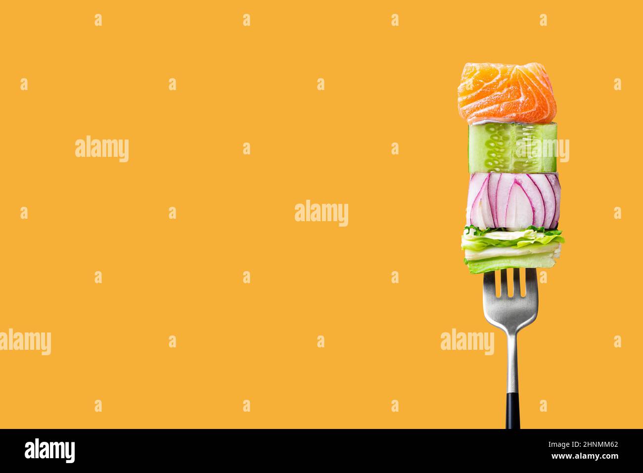 fork with food on it: delicious fillet salmon, cucumber, onion, green salad on orange background Stock Photo