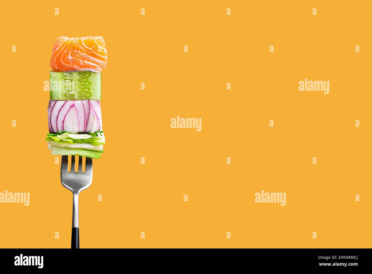 fork with food on it: delicious fillet salmon, cucumber, onion, green salad on orange background Stock Photo