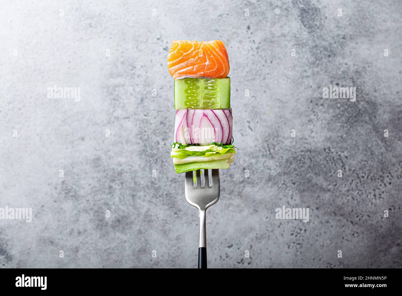 fork with food on it: delicious fillet salmon, cucumber, onion, salad on gray stone rustic background Stock Photo