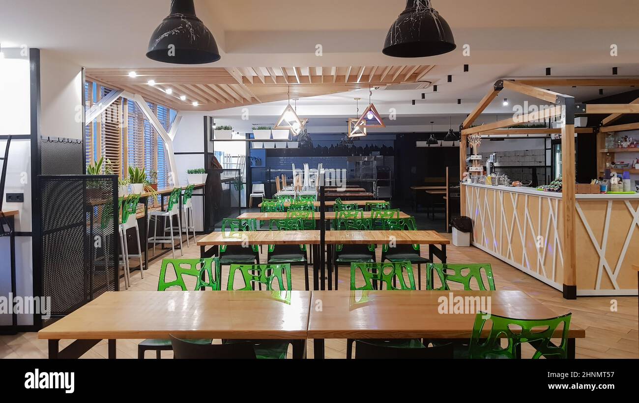 Cafeteria, no people dining room with wooden tables and green chairs. Interior with wood and metal elements. Modern dining areas with window lighting. Ukraine, Kiev - February 19, 2021 Stock Photo