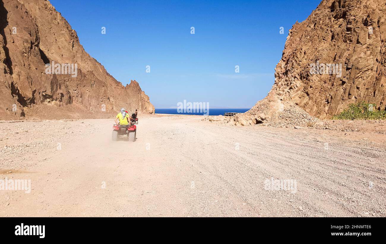 Desert in Egypt. Rocky sand hills. A lone tourist on an ATV in the desert against the background of blue sky and mountains is walking towards the Red Sea. Landscape in the desert. Stock Photo