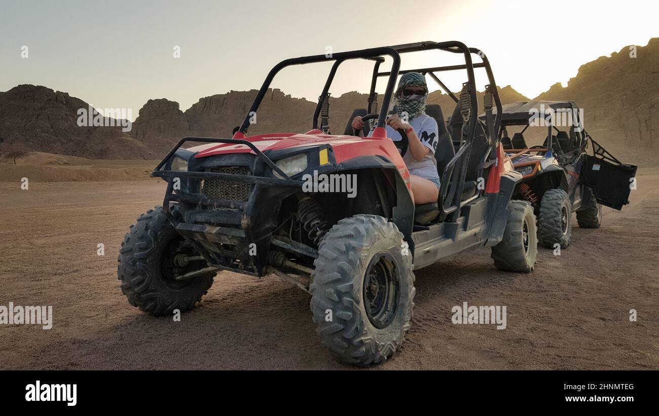 Egypt, Sharm El Sheikh - October 10, 2020. Active woman driving an ATV on a dirt road in the desert against the backdrop of rocky sandy mountains in the sunset. Stock Photo
