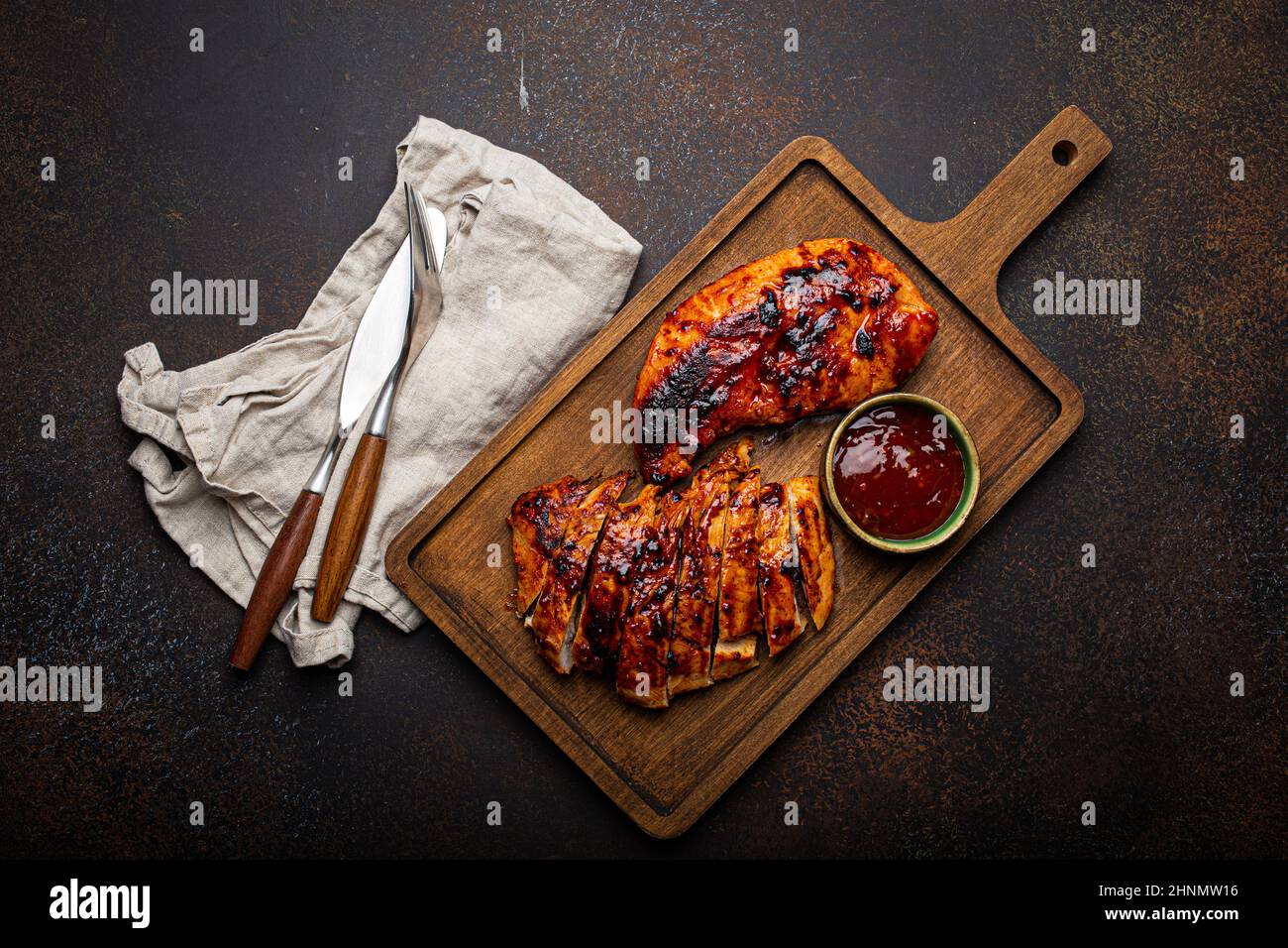 Grilled turkey or chicken fillet with red sauce served and sliced on wooden cutting board Stock Photo