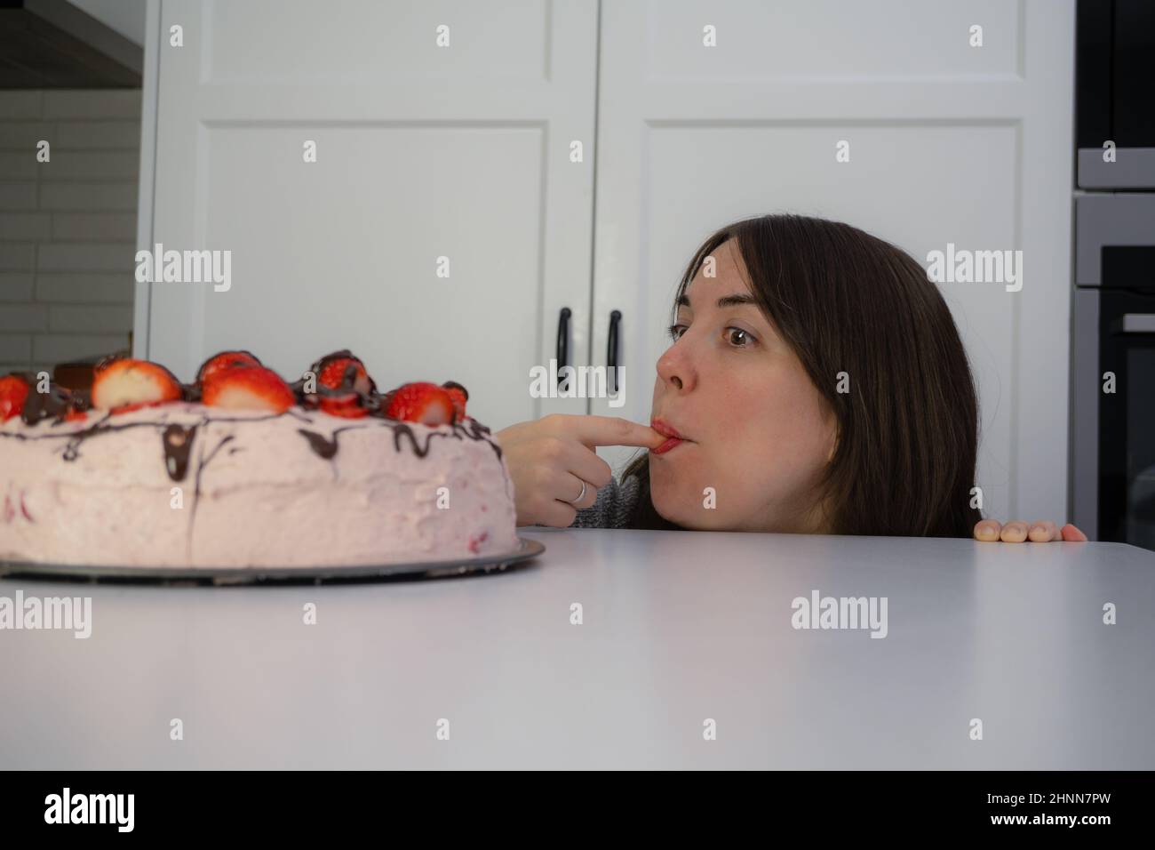 young girl eating a cake hidden behind a table in the kitchen of her home  with copi-space Stock Photo - Alamy