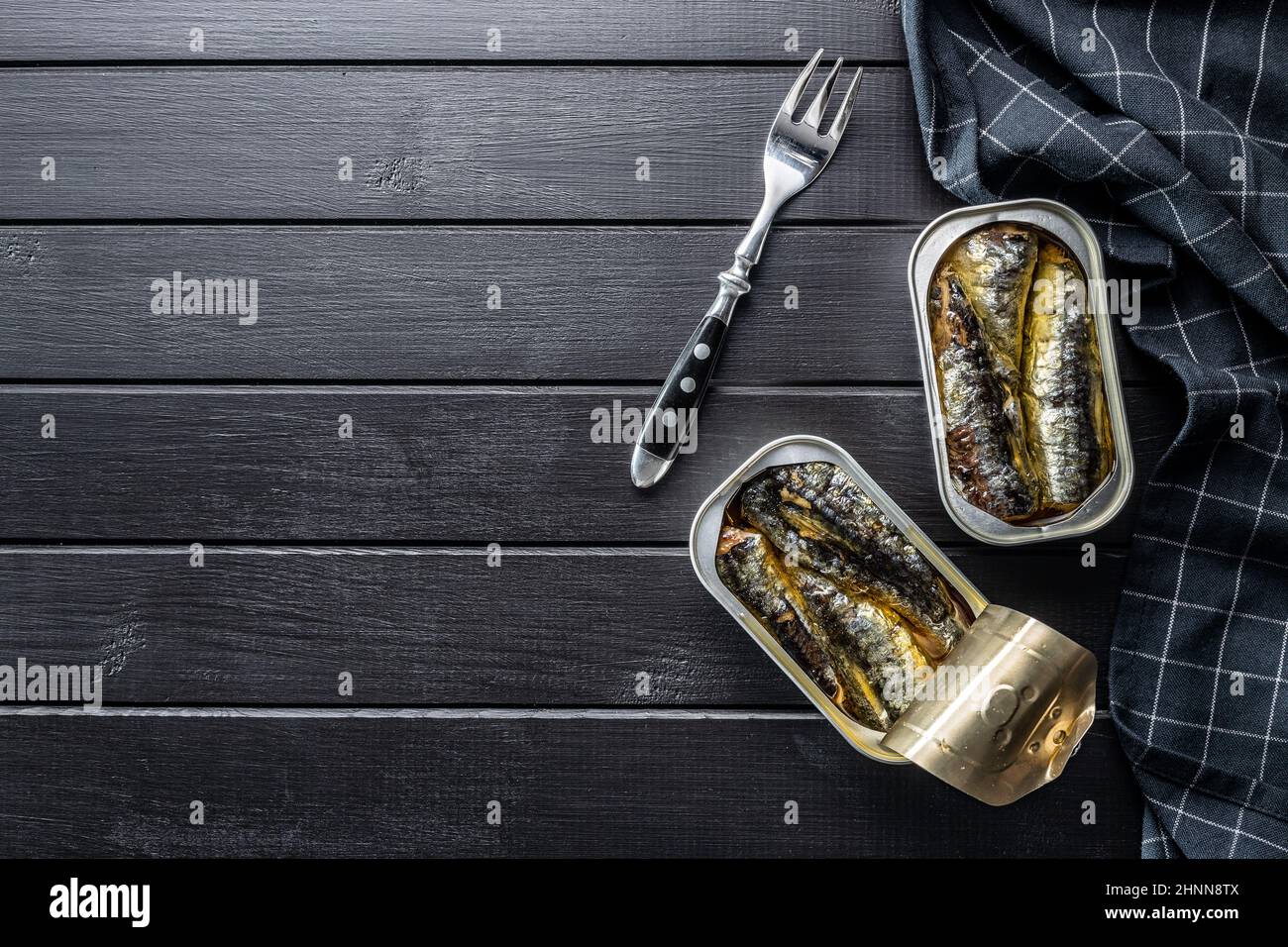Canned sardines. Sea fish in tin can on black table. Top view Stock