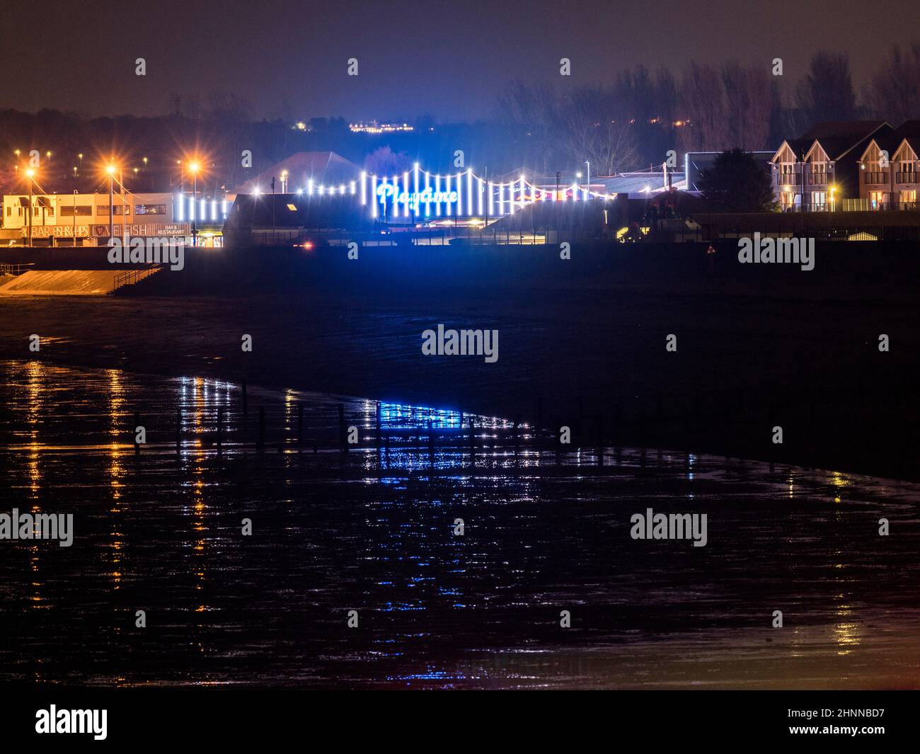 Warden Bay, Kent, UK. 17th Feb, 2021. UK Weather: colourful arcade properties in Leysdown seen reflected from Warden Bay in a brief period of calm before Storm Eunice. Credit: James Bell/Alamy Live News Stock Photo