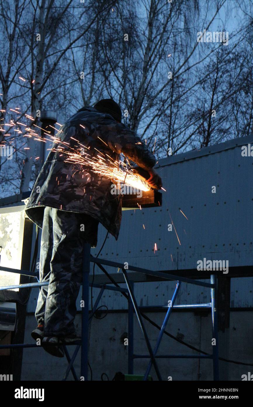 worker cuts metal, sheaf of bright sparks scatter in the twilight Stock Photo