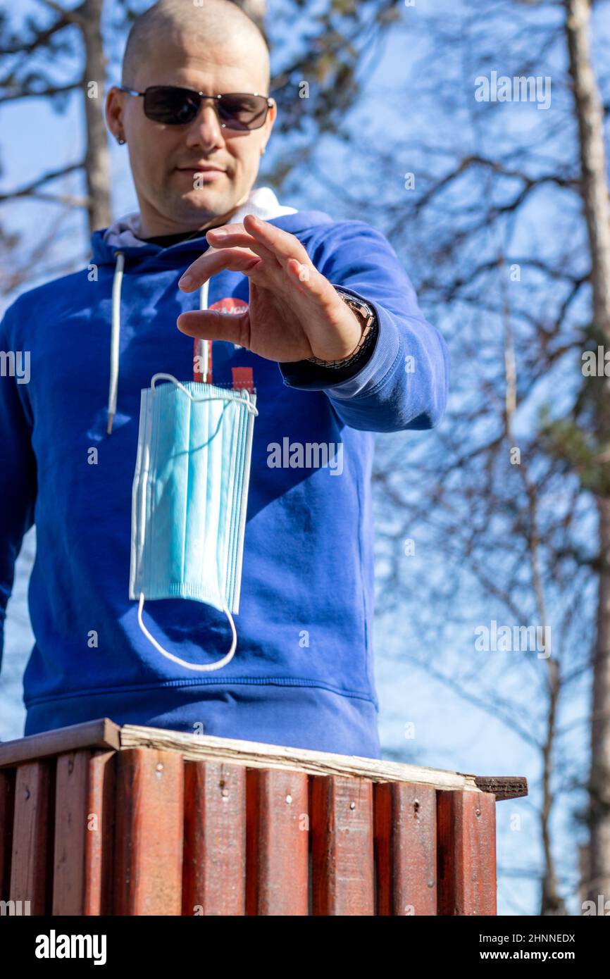 A young man in the park threw away a protective face mask into the trash bin. Covid-19 pandemic crisis end. Stock Photo