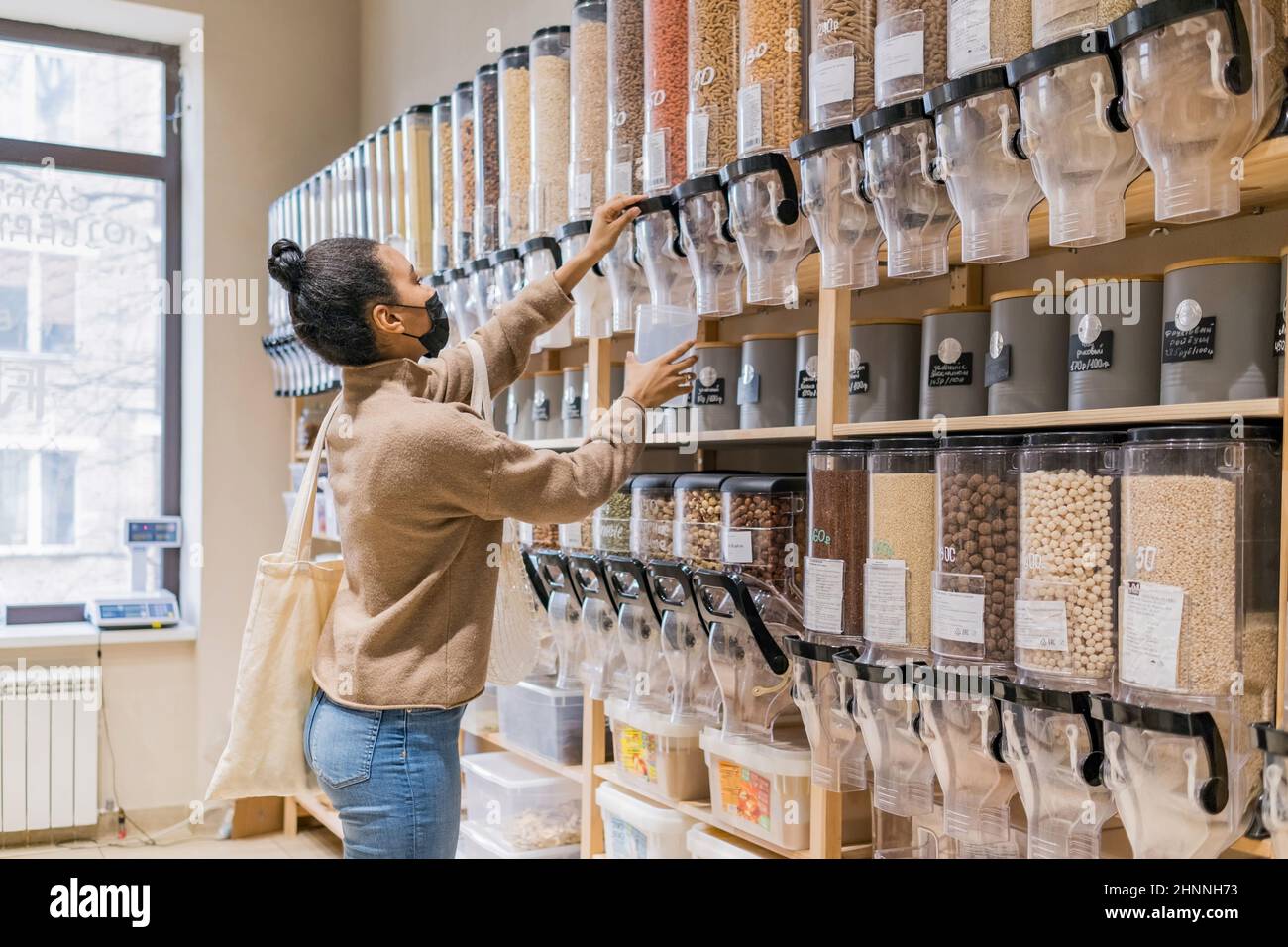 Young african american woman wearing mask buying cereals and grains in sustainable zero waste grocery store Stock Photo
