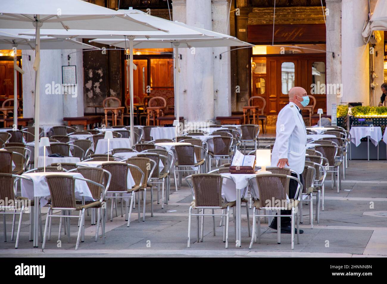 waiter waits for customer at famous cafe Floria at St. Mark's square in Venice. He wears a face mask to protect agsinst covid 19 Stock Photo