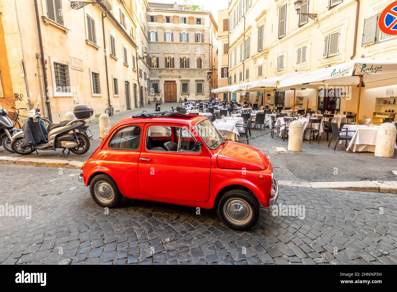 vintage Fiat 500 parked next to a restaurant in Rome in the inner city at quarter Regla on cobblestone street. The world famous Italian automobile brand founded in 1899. Stock Photo