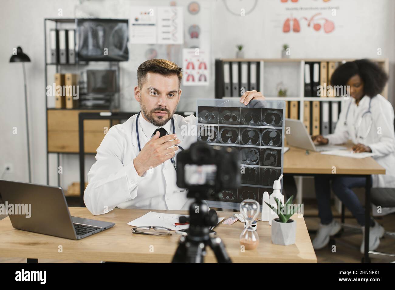 Caucasian medical specialist with x ray in hands talking and gesturing while filming new video for his blog. Concept of people, technology and health care. Stock Photo