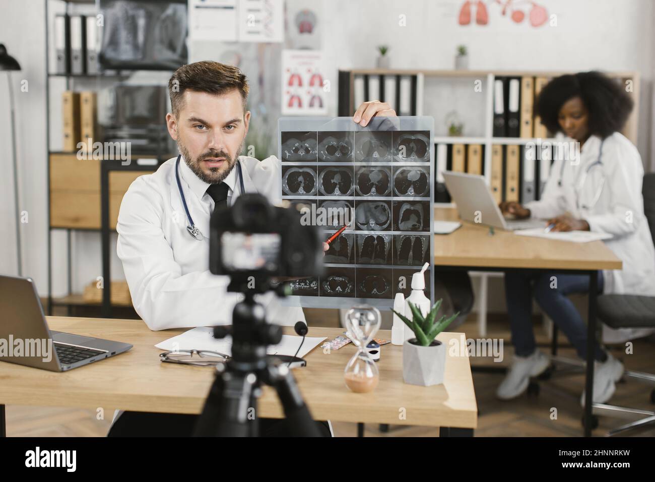 Caucasian medical specialist with x ray in hands talking and gesturing while filming new video for his blog. Concept of people, technology and health care. Stock Photo