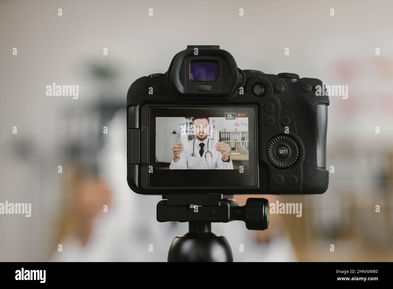 Video camera screen with qualified medical worker sitting at hospital room and talking about various pills. Video consultation and broadcast concept. Stock Photo