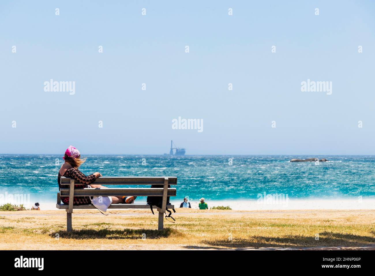 Woman on bench on the extremely windy beach, Camps Bay. Stock Photo