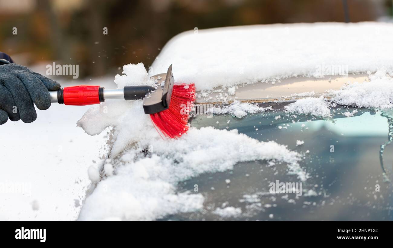 Human hand cleaning car from snow in wintertime day. Person in gloves