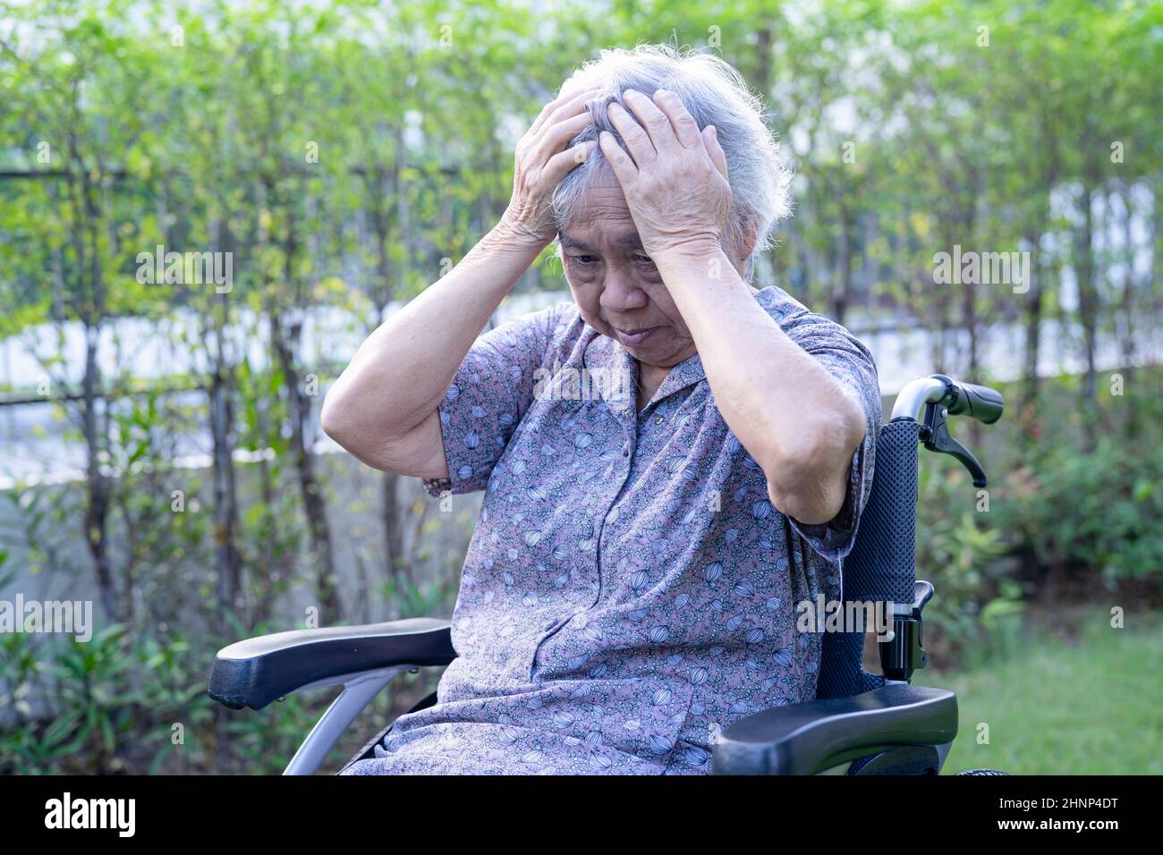 Asian senior or elderly old lady woman patient headache while sitting on bed in nursing hospital ward, healthy strong medical concept Stock Photo