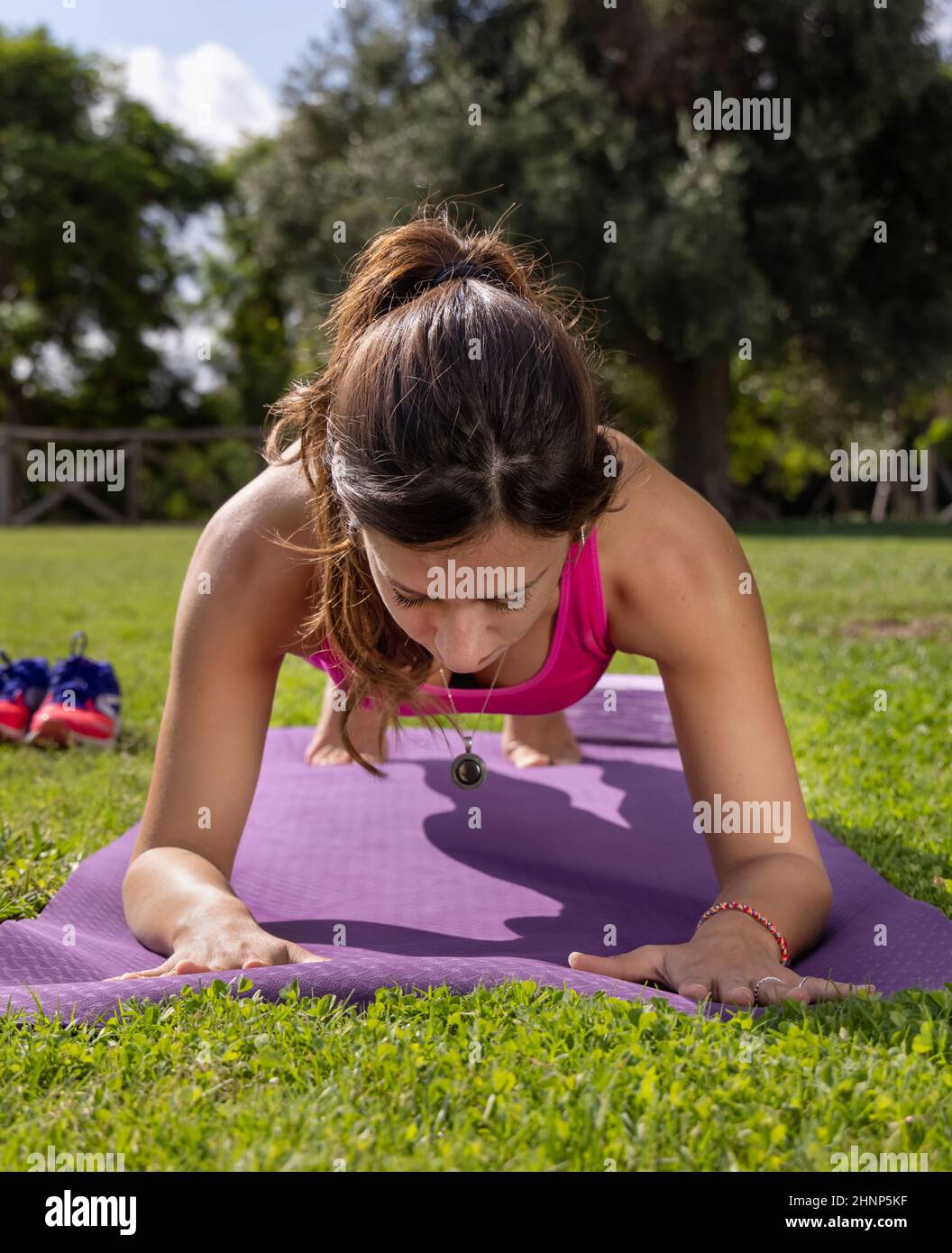 Young concentrated woman in plank position on mat in a park in a summer day Stock Photo