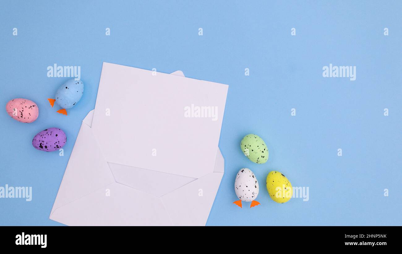 Paper card note in envelope with Easter eggs on bright pastel blue background. Creative copy space flat lay composition Stock Photo