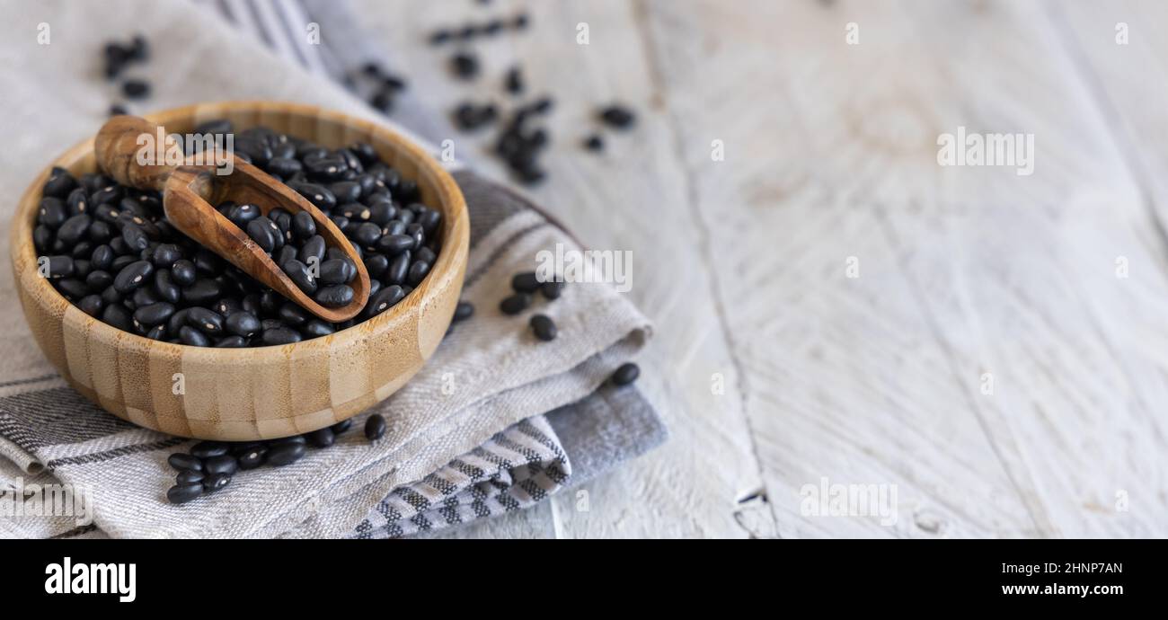 Wooden bowl full of dried black beans with a wooden spoon on kitchen