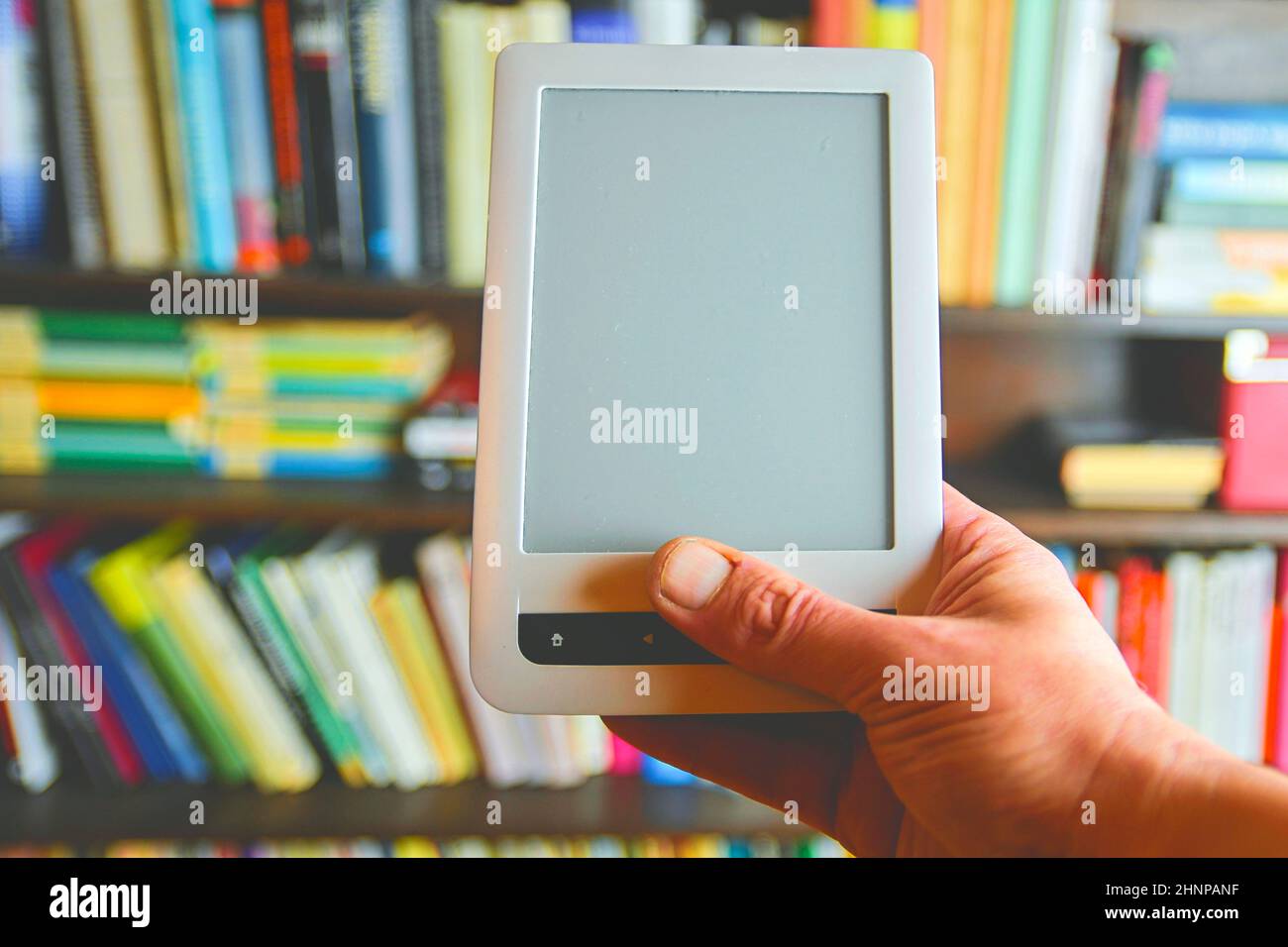Ebook or digital reading tablet device. E-book in man's hand.  On the background is the shelf with bright real books. Online shopping books concept Stock Photo