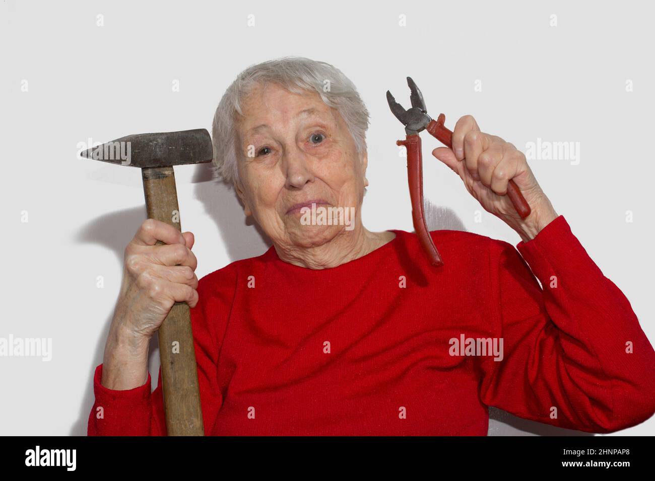 Funny portrait of senior woman holding hammer and pliers in his hand isolated on white Stock Photo