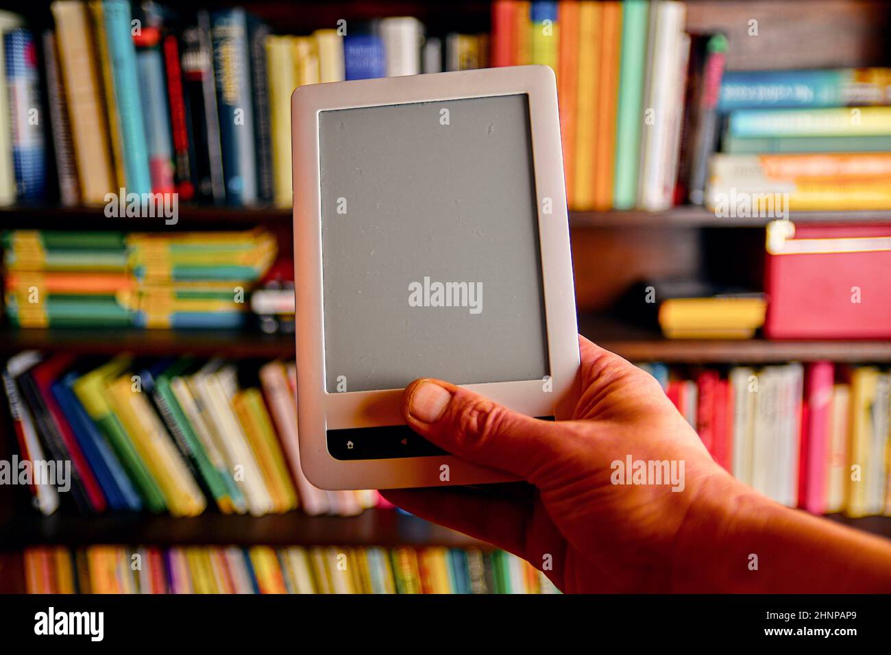 Ebook or digital reading tablet device. Ebook in man's hand. On the background is the shelf