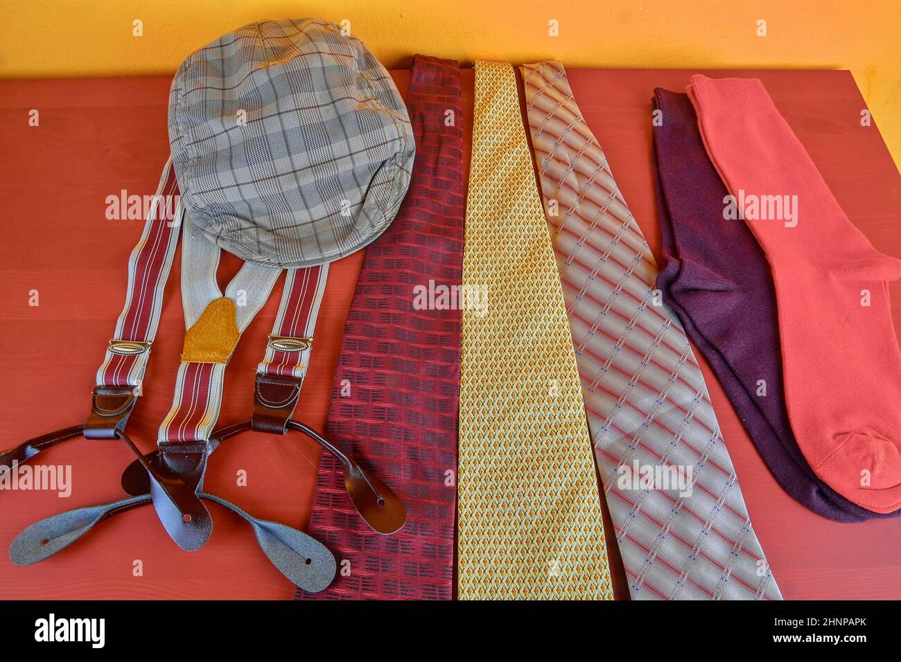 Man garments. Clothing concept for men. Colorful socks, ties, braces and checked flat cap on claret background. Classical concept of men garments. Close-up Stock Photo