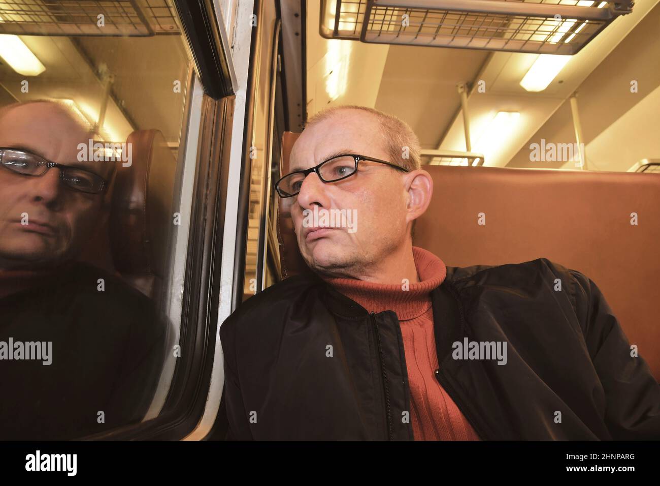 Middle age man looking out of the window of train. Passenger during travel by high speed express train in Europe. Elderly man travelling in train at night Stock Photo