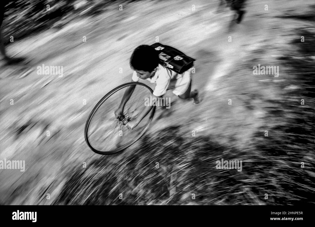 boy in school uniform runs back home playing with a wheel of a bicycle Stock Photo