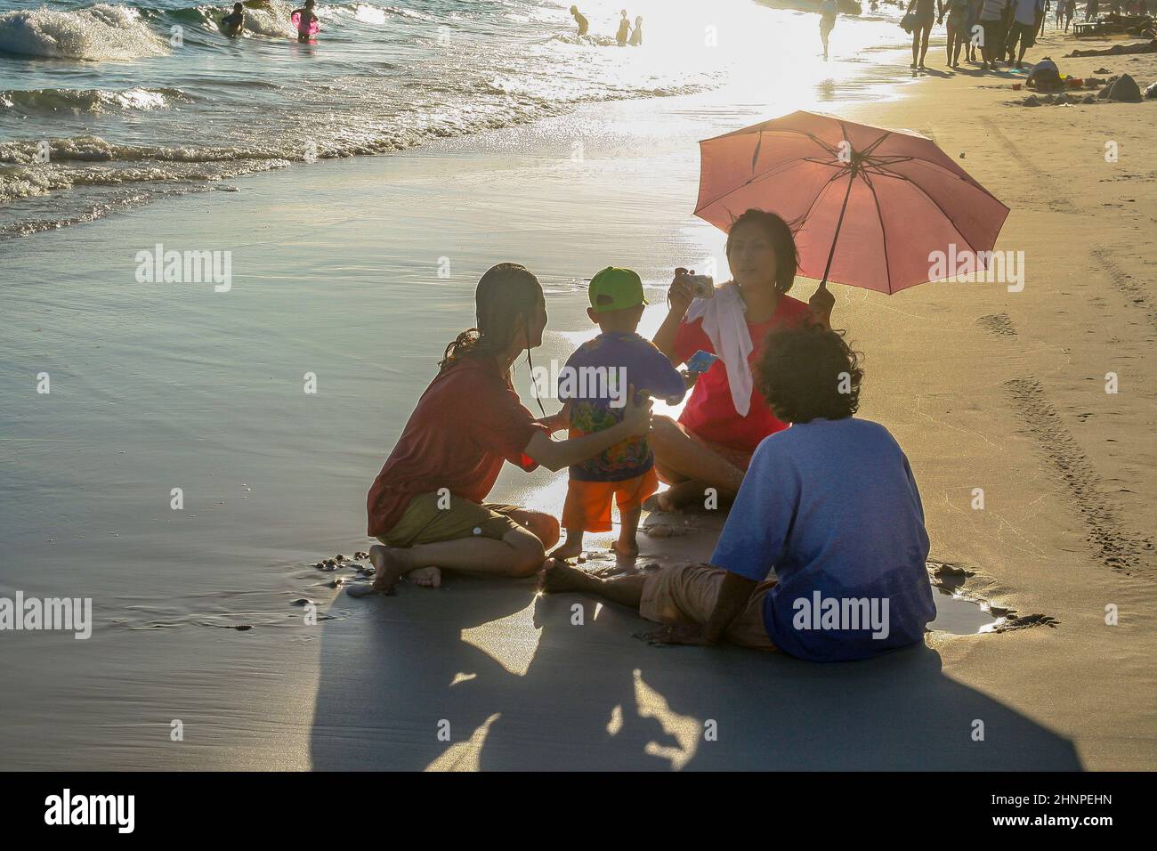 amily relaxes at the beach in Koh Samet in sunset. equipped with umbrella for sun protection they sit togethter at the beach. Stock Photo