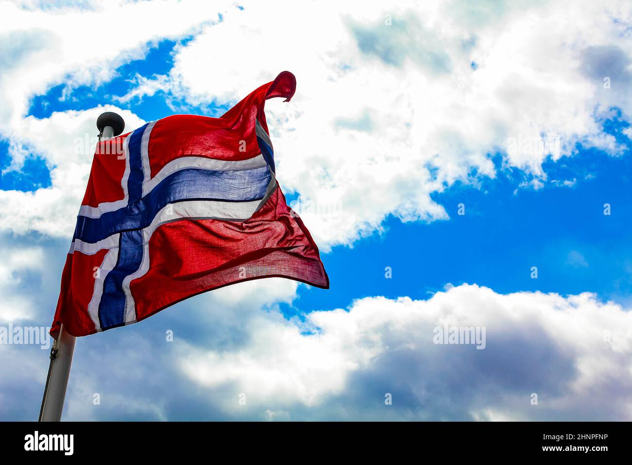 The national flag of Norway in the rough wind and blue sky with clouds ...
