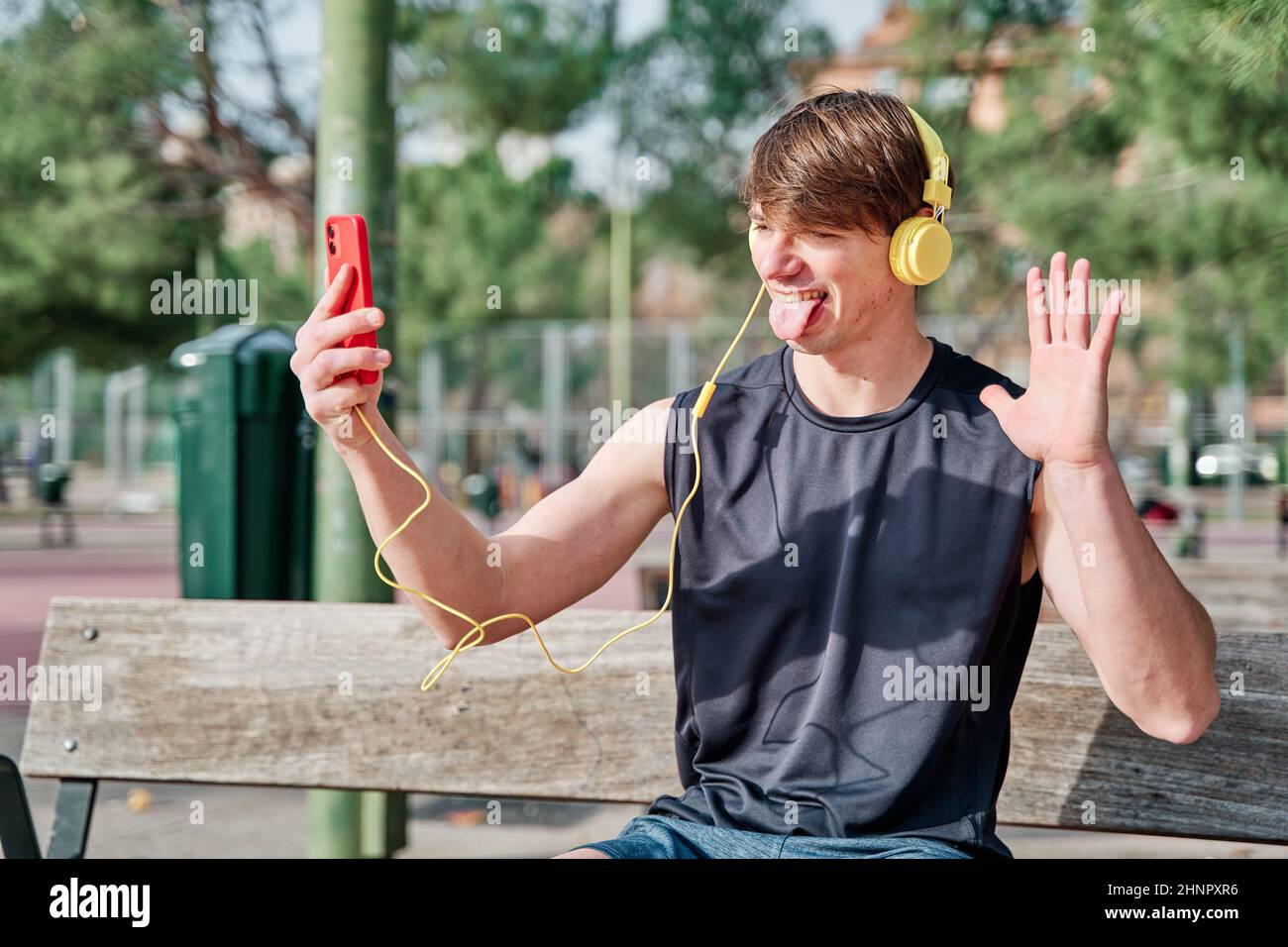 Cheerful young sportsman making video call on his smartphone with earphone - young fit male taking a selfie after exercising Stock Photo