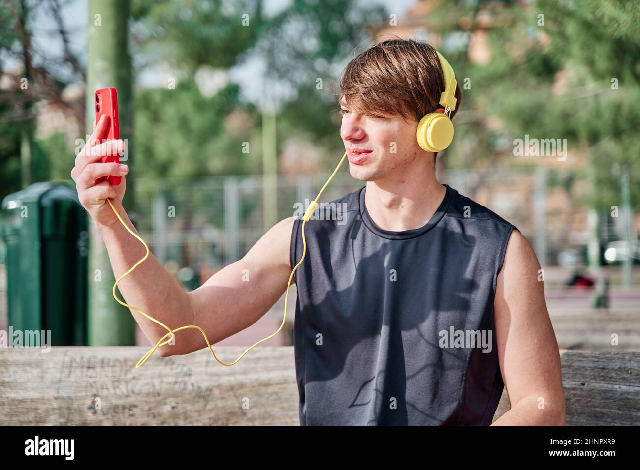 Cheerful young sportsman making video call on his smartphone with earphone - young fit male taking a selfie after exercising Stock Photo
