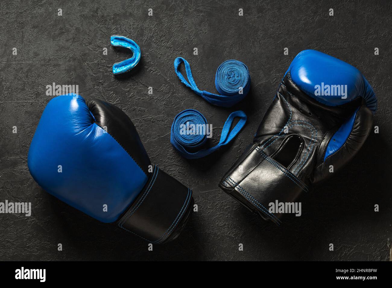 Boxing gloves with mouthguard and blue boxing bandages on a black background. Stock Photo